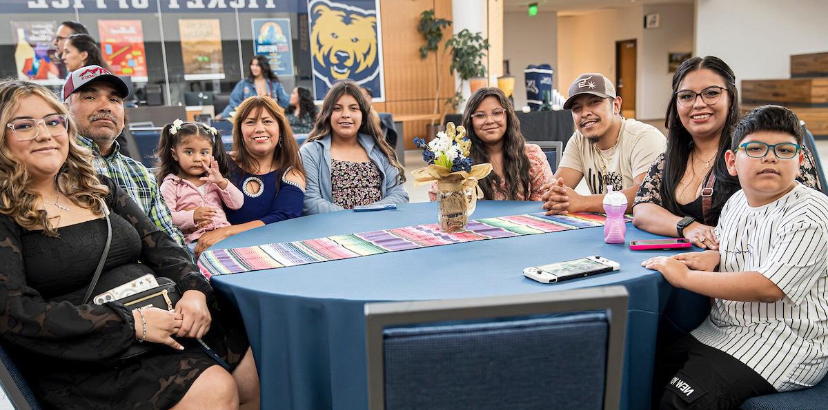 family siting on a table with blue tablecloth, at the back the bear of UNC called Klawz